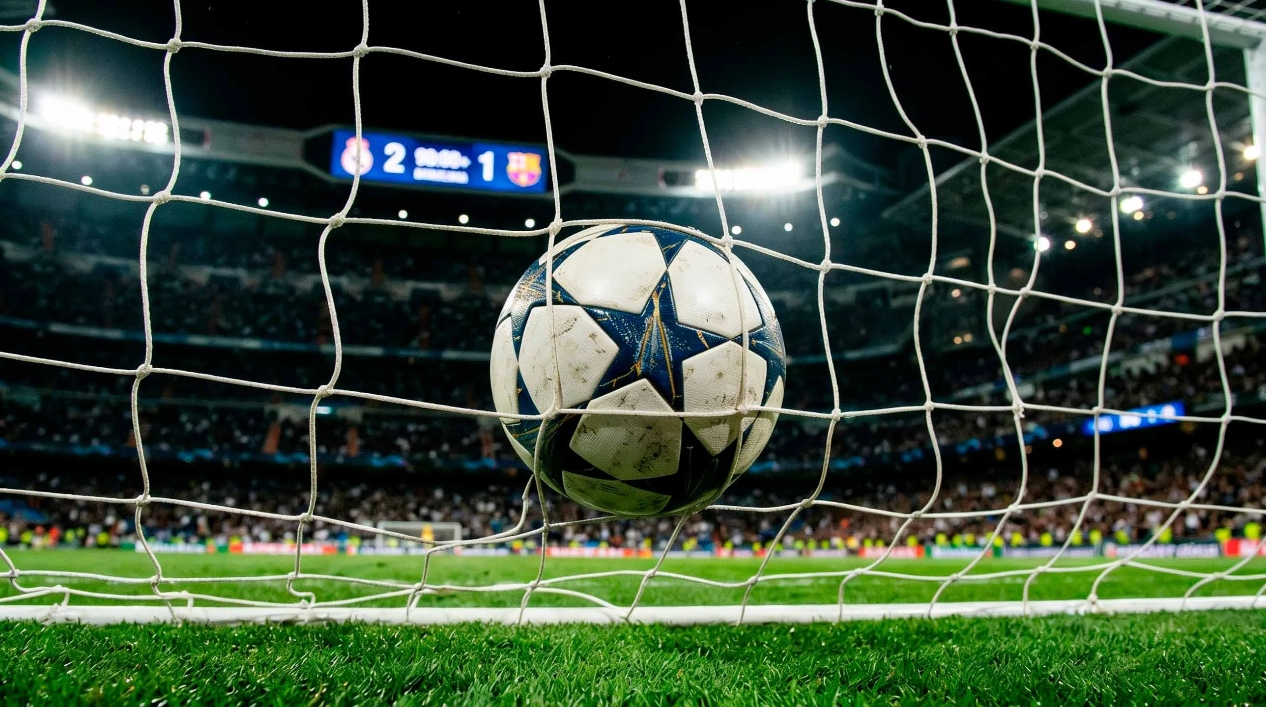 Balón de fútbol de la Champions League dentro de la red de una portería con el marcador iluminado al fondo